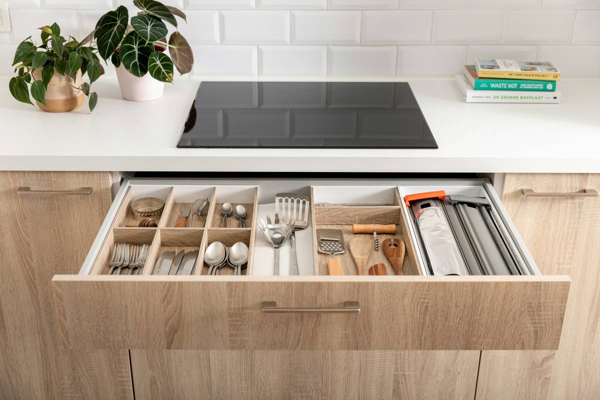 Before and after images of a kitchen drawer: left side shows chaotic jumble of utensils; right side shows neatly arranged compartments using small bamboo boxes.